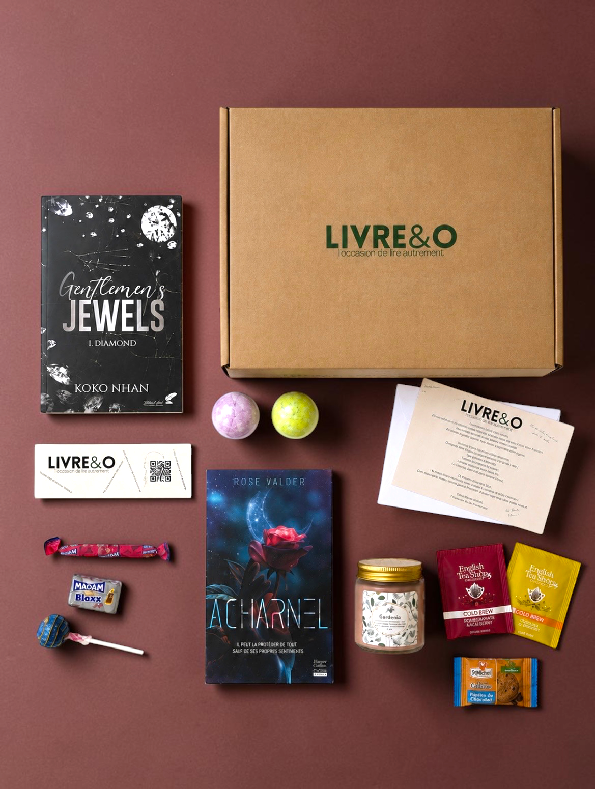 Box Découverte Romance LIVRE&O contenant des romans, des thés, des douceurs et une bougie sur fond bordeaux