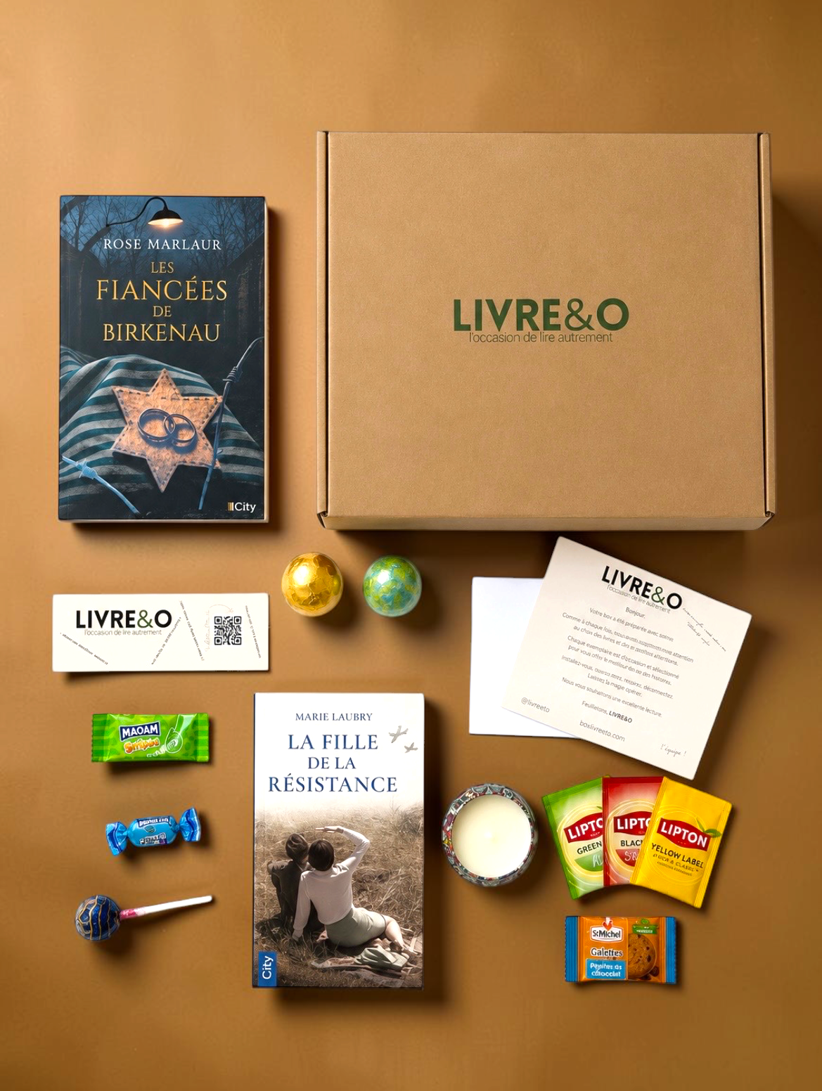 Box découverte LIVRE&O contenant deux romans historiques, des gourmandises, du thé et une bougie sur fond beige