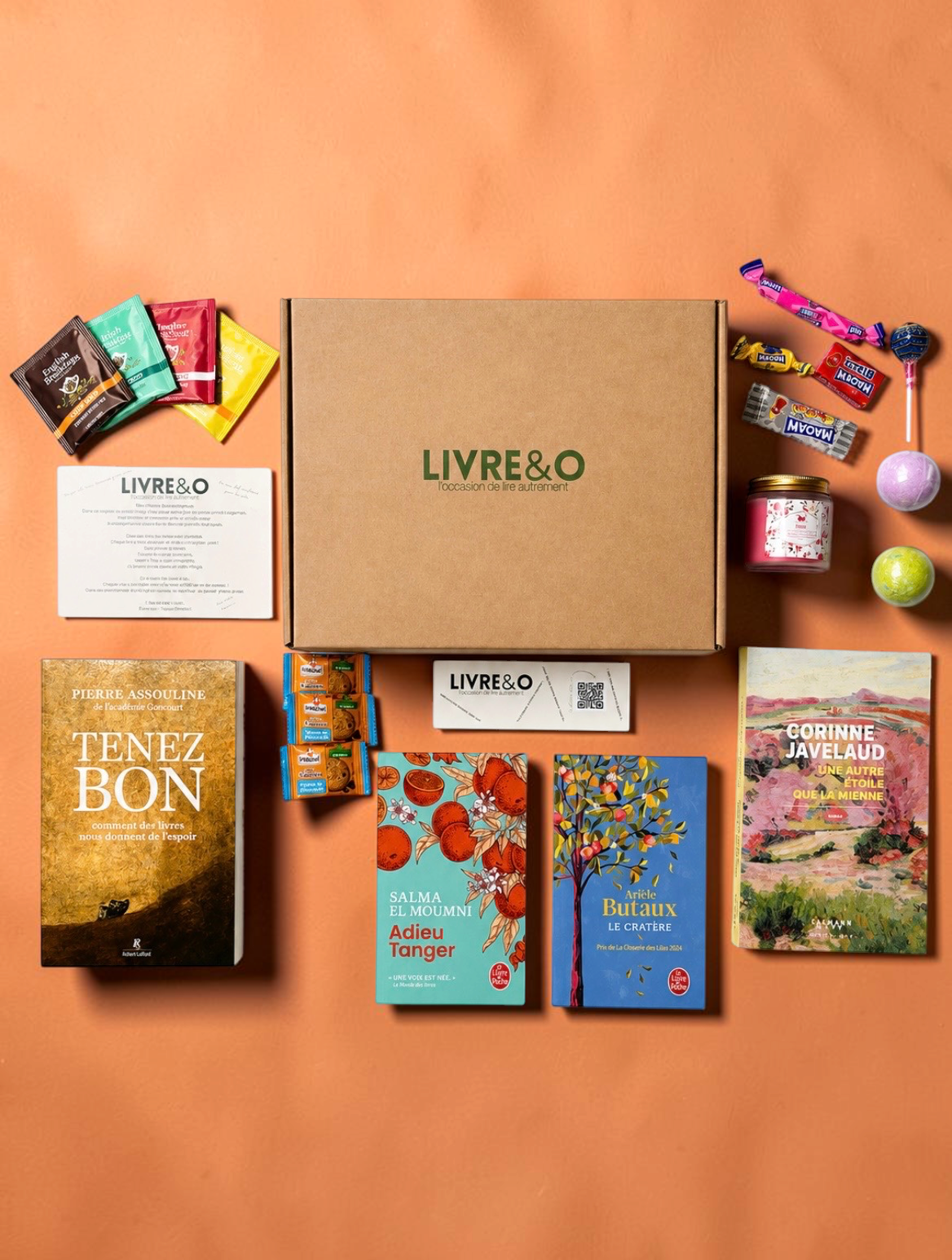 Box littéraire LIVRE&O contenant quatre romans, des gourmandises, une bougie et des sachets de thé sur fond orange