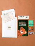 Enveloppe LIVRE&O contenant un roman broché, un marque-page, du thé et des gourmandises sur fond beige.