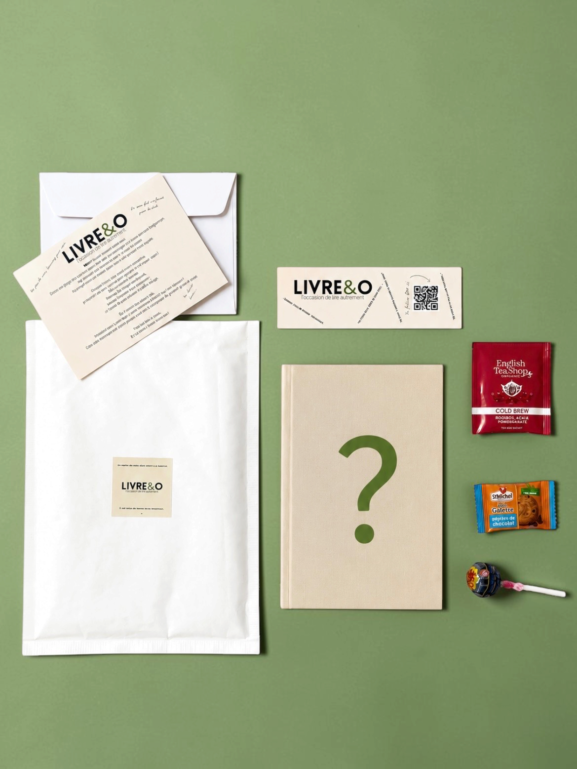 Enveloppe surprise LIVRE&O contenant un livre broché, un marque-page, des gourmandises et une carte explicative.