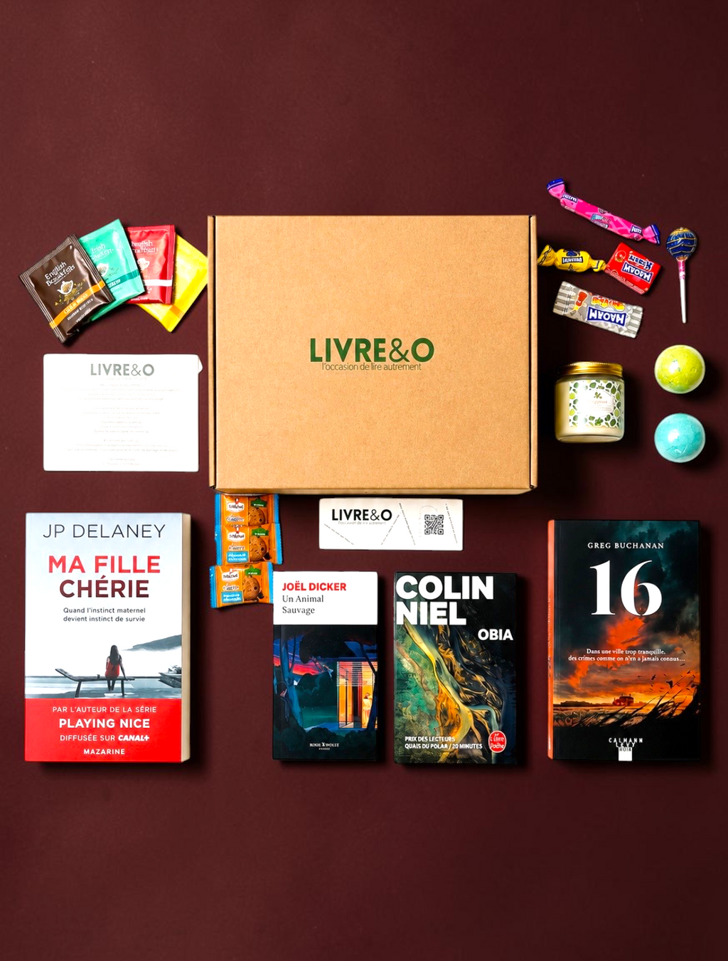 Box LIVRE&O contenant quatre romans noirs, des sachets de thé, des friandises et une bougie parfumée sur fond blanc.