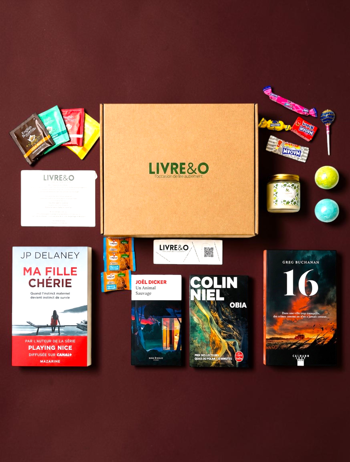Box LIVRE&O contenant quatre romans noirs, des sachets de thé, des friandises et une bougie parfumée sur fond blanc.