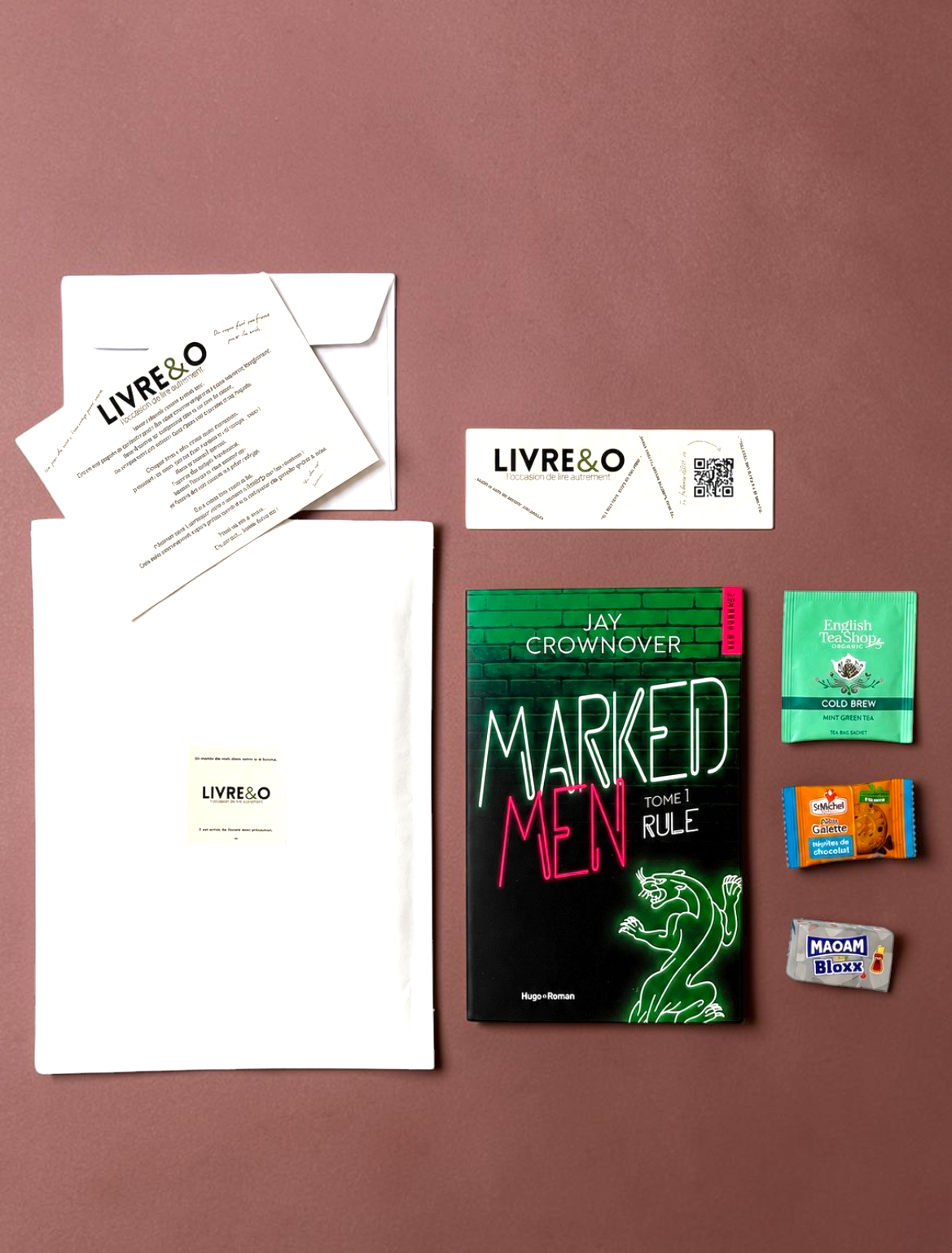 Enveloppe LIVRE&O Romance contenant un roman broché, un marque-page, du thé et des gourmandises sur fond rose